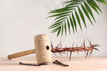 Crown of thorns with wooden hammer, nails and palm leaf on beige grunge table against white...