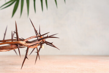Crown of thorns with palm leaf on beige grunge table against white background, closeup. Good Friday...
