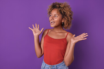 Young overjoyed African American woman teen spreads arms to sides seeing friend and rejoicing at long-awaited meeting after separation on summer vacation stands in purple studio. Schoolgirl, student