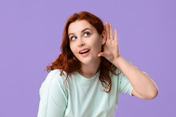 Beautiful young redhead woman showing eavesdrop gesture on lilac background