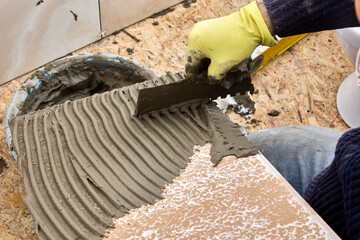 Tiler spreads cement mortar onto tile surface using notched trowel.