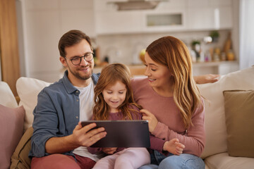 Curious little girl using the tablet with her parents in the living room