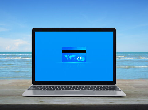 Credit card on modern laptop computer monitor screen on wooden table over tropical sea and blue sky with white clouds, Online e-payment concept, Elements of this image furnished by NASA