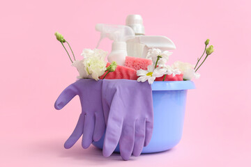 Basin with cleaning supplies, tools and spring flowers on pink background