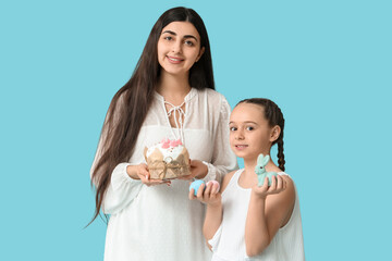 Happy smiling young woman and her daughter with Easter cake and toy bunny on blue background