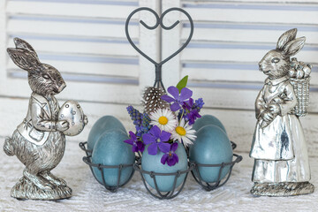 Oster-Arrangement mit Osterhasen und blau gefärbten Eiern dekoriert mit Frühlingsblumen