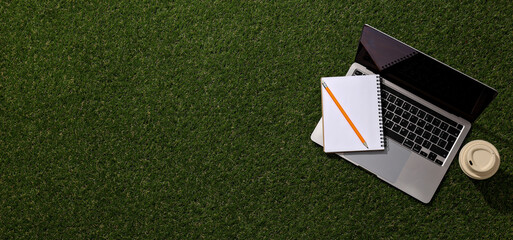 Laptop with notebooks on the grass, top view.