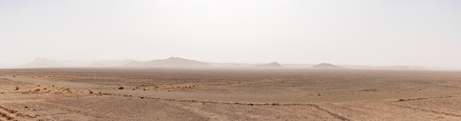 Fototapeta na wymiar panorama desert landscape with arid hlls in the distance under a hazy sandstorm sky in southern Morocco