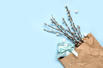 Paper bag with pussy willow branches, Easter eggs and gift box on blue background