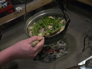 Big pot of Akita famous Mountain nabe soup of mushroom and yam hanging over the glowing coals in irori traditional hearth