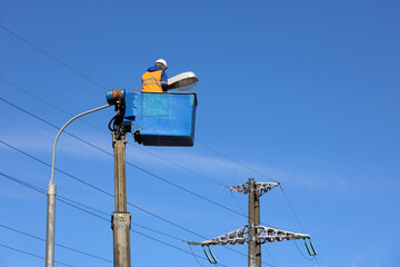 Electrician repairing the street light. Worker on the lifting platform near the lantern against the blue sky	