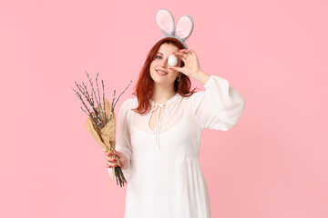 Beautiful young woman in bunny ears with pussy willow branches and Easter egg on pink background