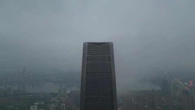 Drone zoom-out shot of a skyscraper with the city behind it, and clouds moving.