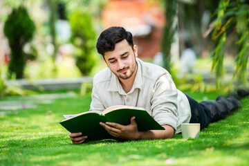 Indian university student reads book in the park over green grass
