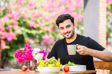 Handsome asian indian man sitting at table outdoors while having coffee, tea or juice