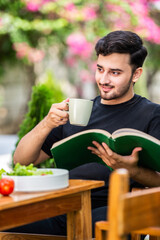 Handsome Indian male student reading book outdoors