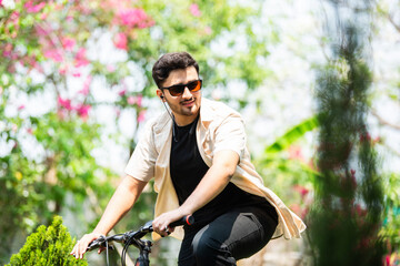 Indian good looking young man rides bicycle and stops for using smartphone