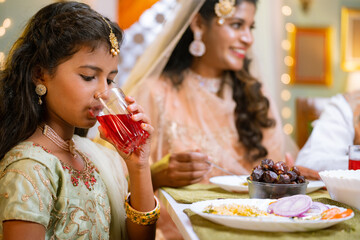 Close up shot of indian girl kid drinking rose soft drinks during ramadan iftar dinner at home -...
