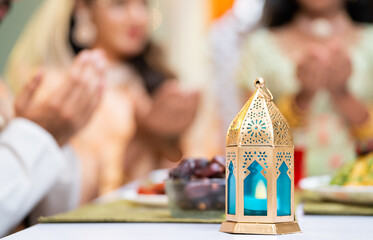 Focus on lantern close up shot of indian muslim couple with kids hands praying during ramadan feast...