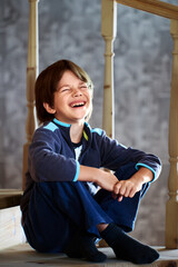 Laughing Caucasian boy, seven years old, sits on an interfloor wooden staircase at home.