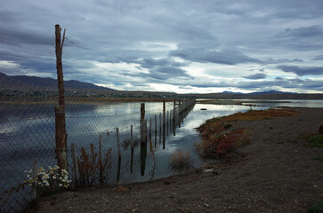 Chain link fence on wooden poles runs through an area flooded with water, Laguna Nimez Nature preserve enclosure near El Calafate, Patagonia, Argentina