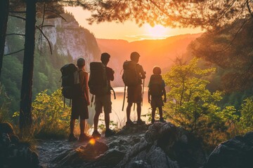 Family of four standing on a rocky outcrop, enjoying a majestic sunset over the mountains. - obrazy, fototapety, plakaty
