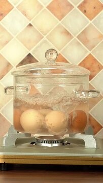 Eggs boiling in a glass pot over a gas stove