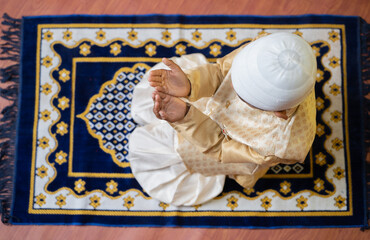 Top view shot of muslim kid doing namaz during ramadan feast celebration at home.