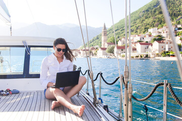 Working in traveling. Happy woman on yacht with laptop. Sea vacation on sailboat in summer. Girl traveler using computer, Internet. Freelancer office workplace outdoors. Successful business lifestyle