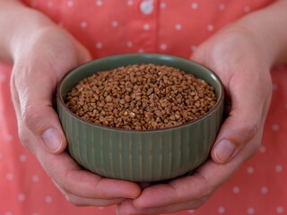 Woman holding green bowl full of buckwheat in her hands.