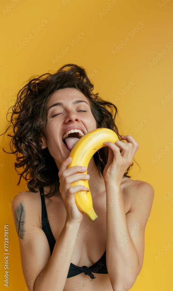 Wall mural Young woman liking a yellow banana