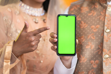 Close up shot of indian muslim couple showing green screen mobile phone by pointing finger at home...