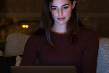 Portrait of young happy woman using laptop at night, using modern technology havinmg fun with glowing screen in dark office or at home, startup business meeting online with businesswoman