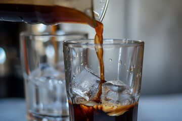 closeup of coffee being poured over ice in a transparent glass