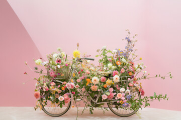 A bicycle with lots of flowers, a floral and greenery installation art piece with a light pink background