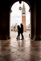 Young couple in love and tourists in front of St. Mark's Square looking at each other in Venice.