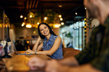 Photo of a smiling businesswoman working online while talking to her male colleague.