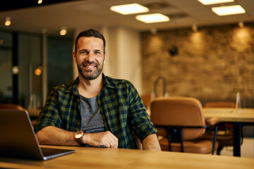 Portrait of a smiling businessman, posing for the camera while sitting and working online at the...