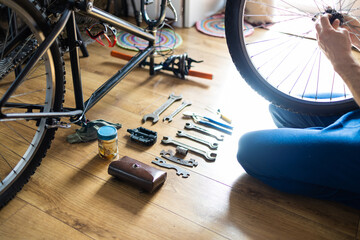Young man repairing a bicycle at home. Mechanic serviceman repairman installing assembling or adjusting bicycle gear on wheel in workshop. - obrazy, fototapety, plakaty