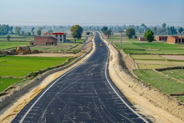 Fototapeta na wymiar New asphalt road through the middle of green farm fields on either side