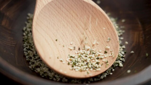 Organic hemp seeds falling on a wooden spoon in rustic kitchen bowl in slow motion. Cannabis sativa purified hulled grains close up. Rotation