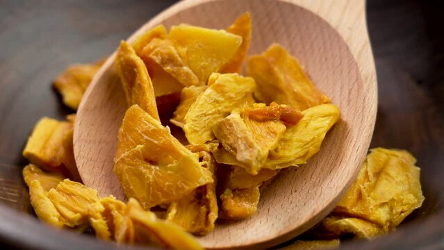 Dried organic mango slices in rustic kitchen dish with wooden spoon close up. Rotation