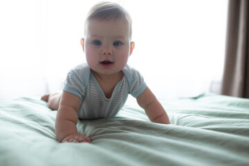 4-5 Monthe old baby lies on a sheet in bed and builds different emotional faces, smileas, studies...