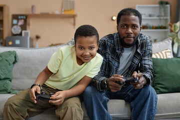 Front view portrait of African American father and son playing video game together and holding...