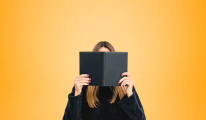 Young woman reading book hiding face, copy space empty background