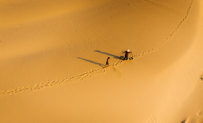 Aerial view of a peasant woman carries a bamboo frame on the shoulder across sand dunes in Ninh...