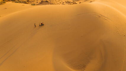 Fototapeta na wymiar Aerial view of a peasant woman carries a bamboo frame on the shoulder across sand dunes in Ninh Thuan province, Vietnam. It is one of the most beautiful places in Vietnam