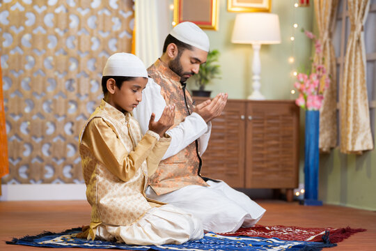 Indian Muslim father with kid doing namaz or praying during ramadan festival celebration at home - concept of ramzan feast, treditions and bonding