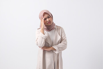 Portrait of overwhelmed Asian hijab woman in casual suit touching her head, having headache, and...