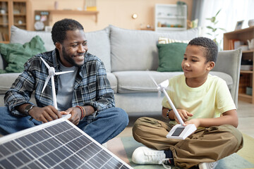 Portrait of smiling African American father and son holding wind turbine model with renewable...